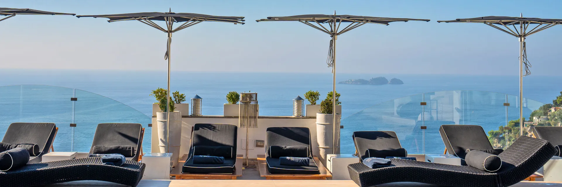 Row of flat dark Tuuci Ocean Master M1 Zero Horizon parasols over sun loungers on a hotel pool terrace overlooking the Mediterranean in Positano