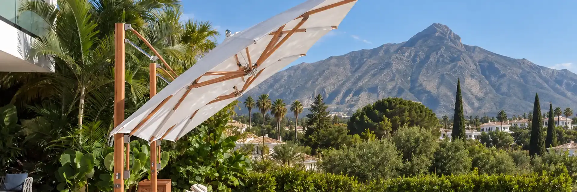Tilted Tuuci Ocean Master MAX cantilever parasol with a teak mast shading loungers beside a villa pool in Marbella, with La Concha mountain behind
