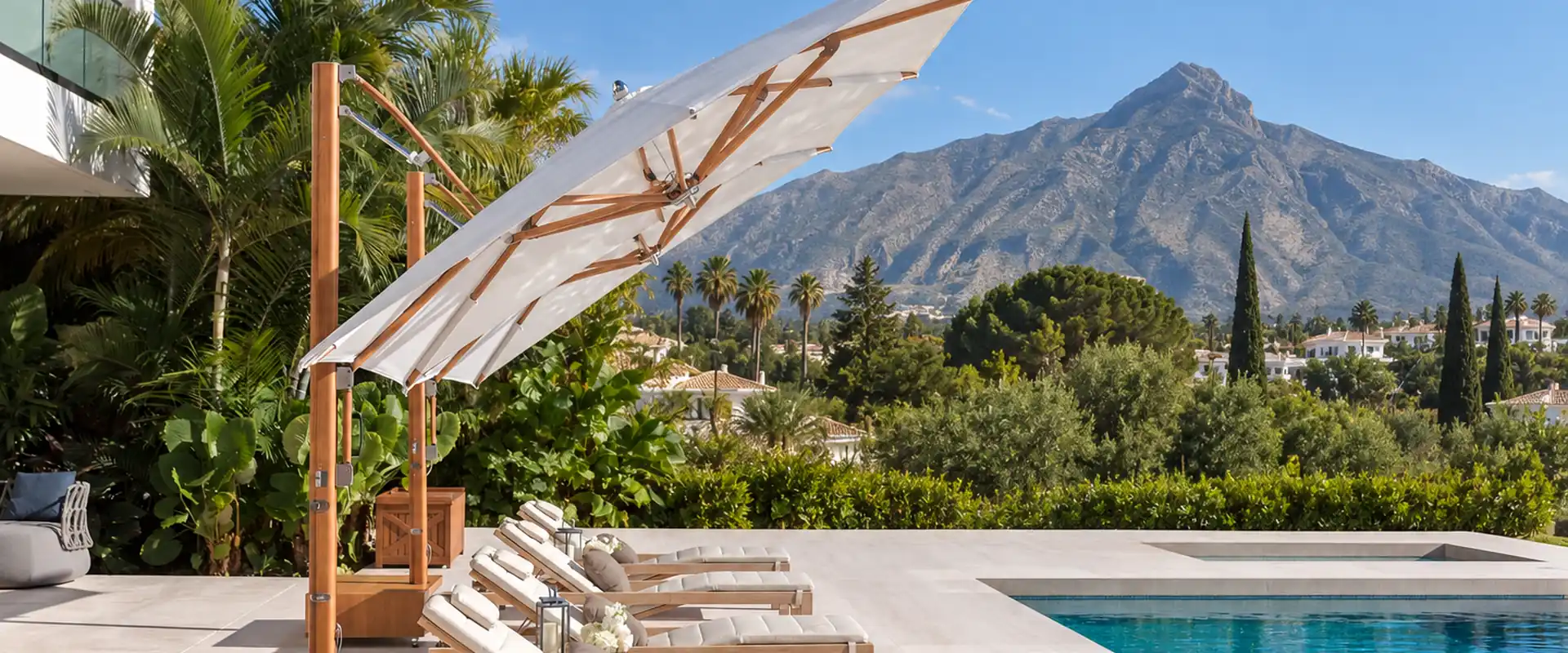 Two white Tuuci Ocean Master MAX Classic Cantilever parasols with teak-finish masts over sun loungers beside a villa pool, with La Concha mountain behind