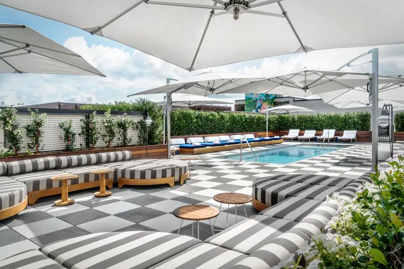 White Tuuci Ocean Master MAX Classic cantilever parasols with polished masts around a rooftop hotel pool, with a chequered floor and striped daybeds