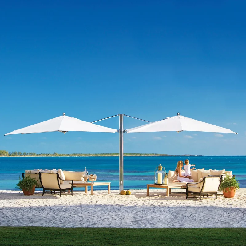 Tuuci Ocean Master MAX Classic Dual Cantilever parasol with two white canopies on a single polished mast, shading lounge seating on white sand in front of a turquoise sea