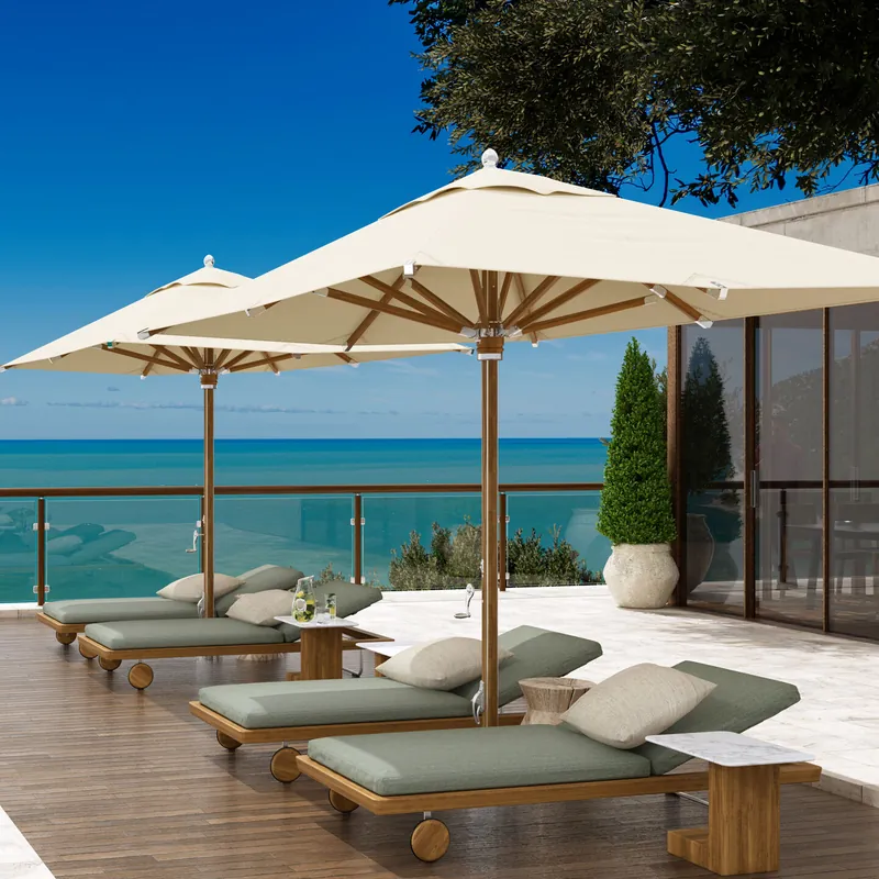 Two cream Tuuci Ocean Master MAX Northstar Nautical Teak center post parasols with teak masts and ribs shading green-cushioned sun loungers on a terrace overlooking the sea