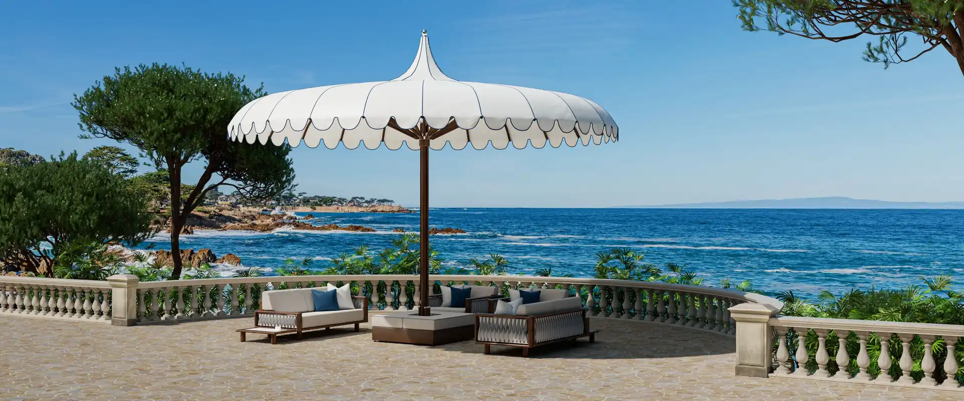 Large white Tuuci Ocean Master MEGA MAX Voilare parasol with a scalloped valance and pointed top shading a group of sofas on a stone terrace with a balustrade, overlooking the sea and pine trees