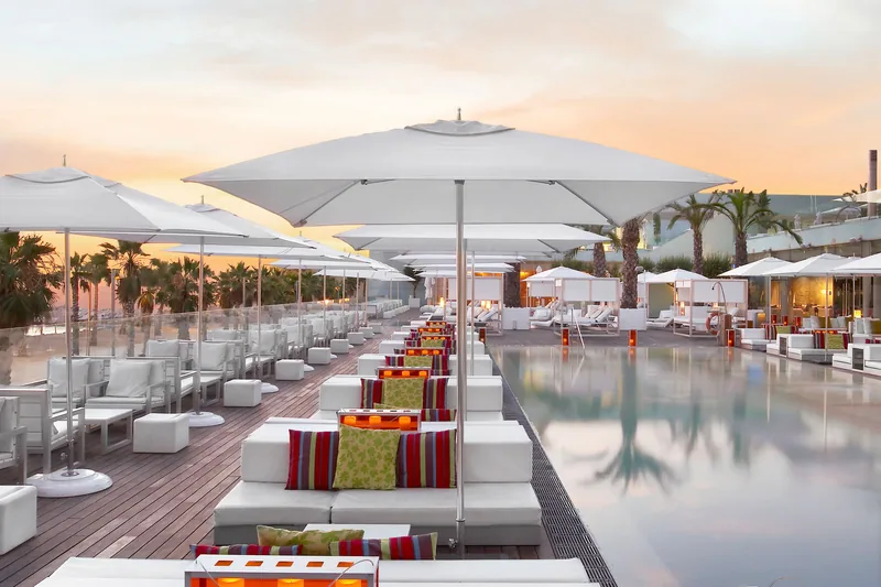 Rows of white Tuuci Ocean Master M1 parasols over a seafront hotel pool terrace in Barcelona at sunset