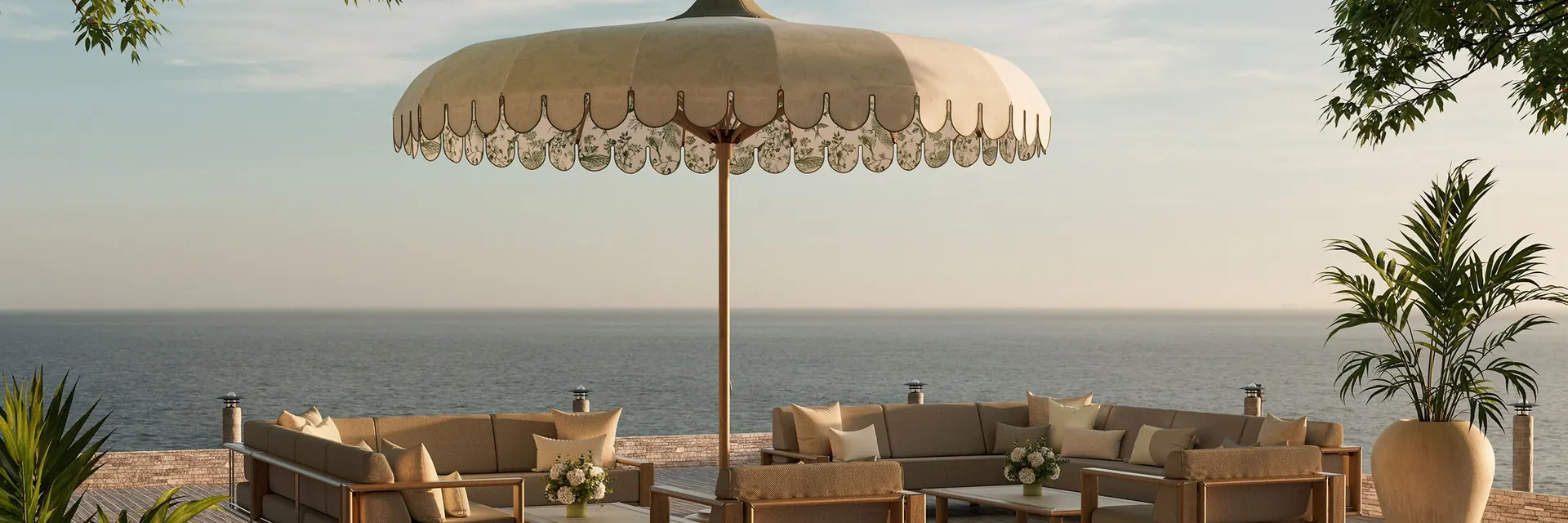 Cream Tuuci Voilare parasol with a botanical-print valance above a teak sectional lounge set on a wooden terrace overlooking the sea