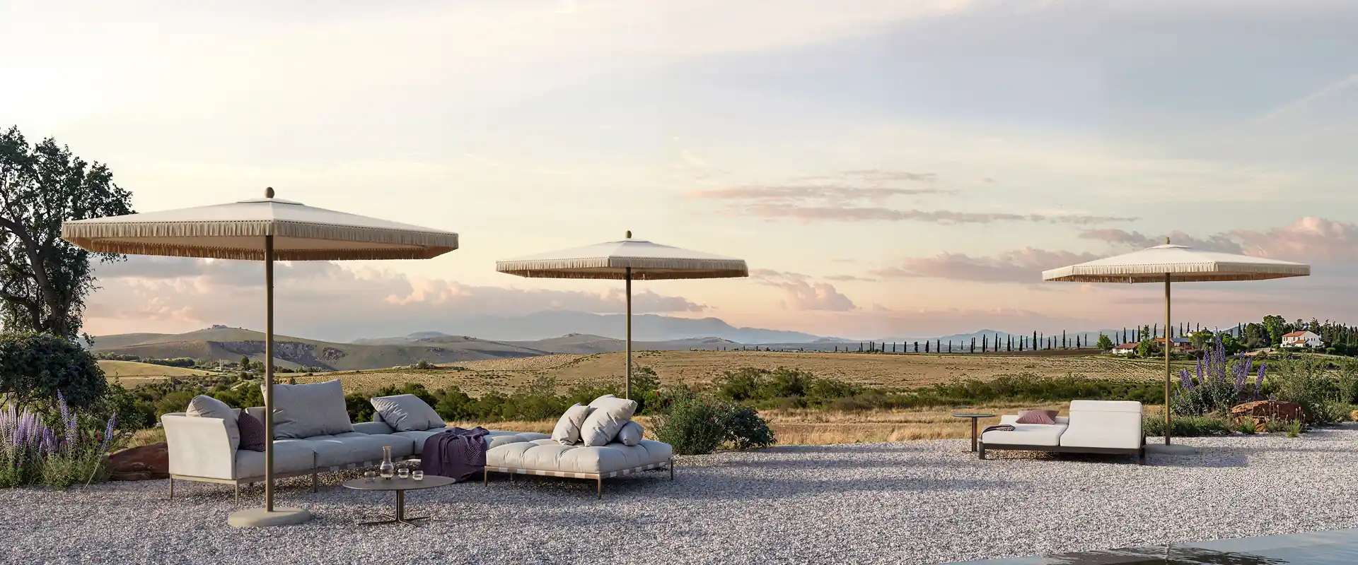 Three Umbrosa Nata UX parasols with fringed canopies over a gravel terrace overlooking rolling countryside