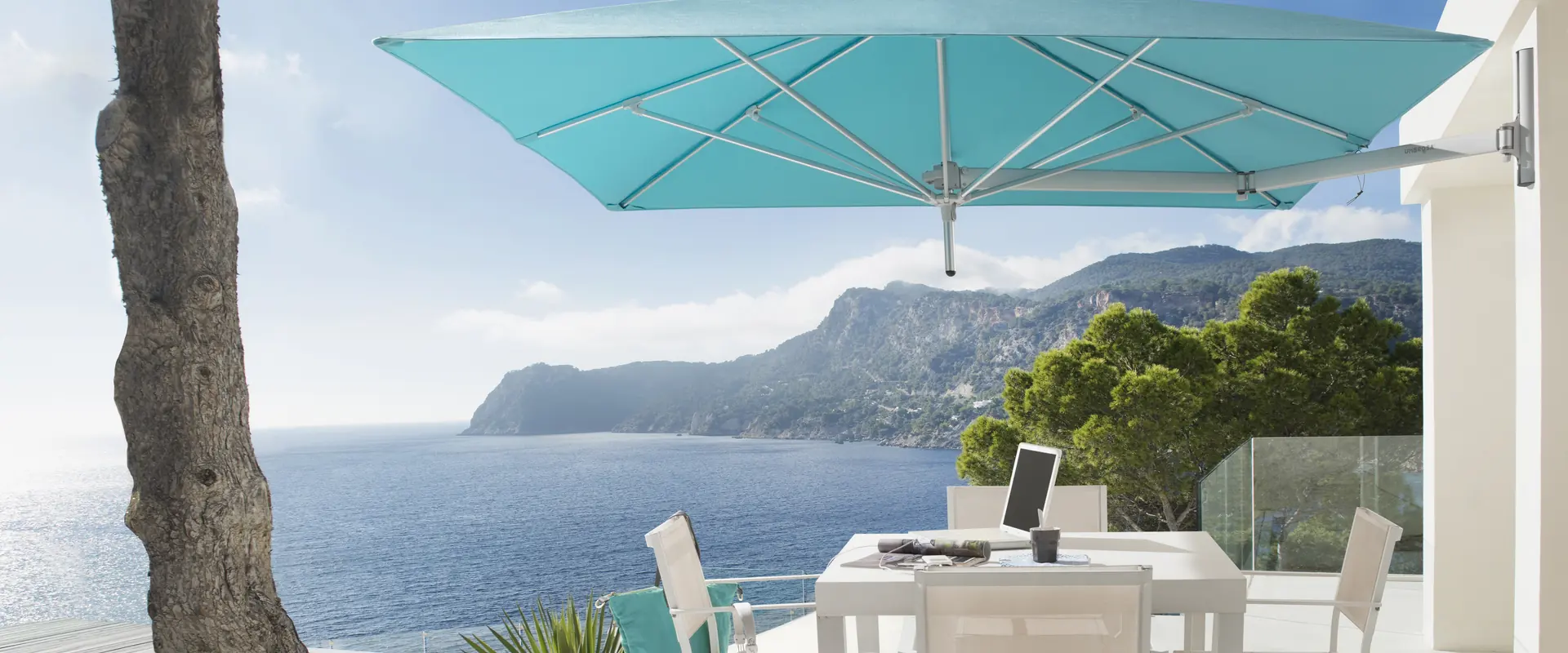 Turquoise Umbrosa Paraflex wall-mounted parasol over a dining table on a sea-view terrace