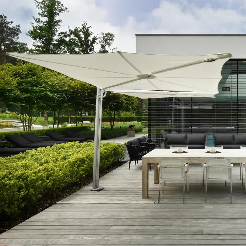 White Umbrosa Spectra cantilever parasol on a slim tilted mast over a dining table on a wooden deck beside a modern villa