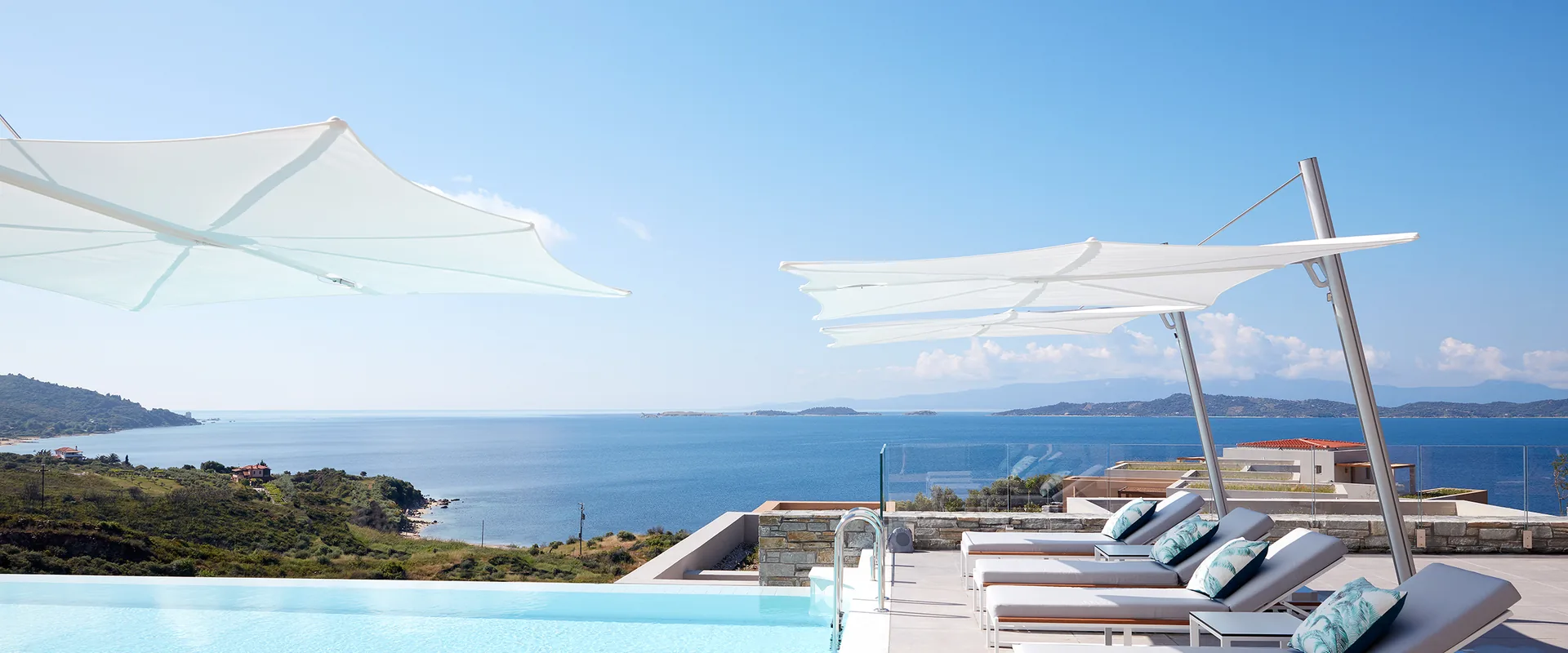 Two white Umbrosa Spectra cantilever parasols above sun loungers beside an infinity pool overlooking the sea
