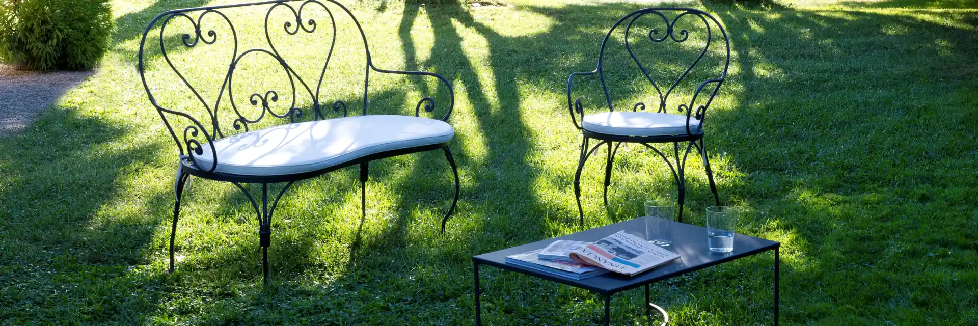 Unopiù Aurora wrought-iron bench and chairs on a lawn in the dappled shade of tall trees