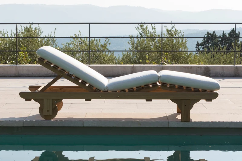 Unopiù Chelsea teak sun lounger with a white mattress on a stone terrace at the edge of a pool, olive trees behind