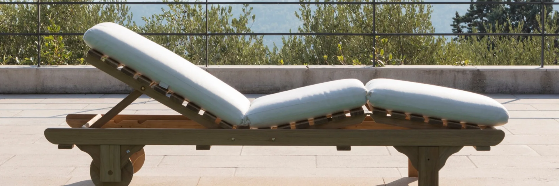 Unopiù Chelsea teak sun lounger with a white mattress on a stone terrace at the edge of a pool, olive trees behind