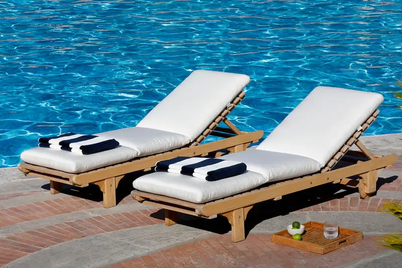 Two Unopiù Chelsea teak sun loungers with white mattresses and rolled towels on a wooden deck beside the sea