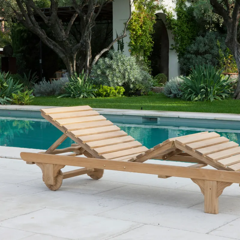Unopiù Chelsea teak sun lounger without a mattress at the edge of a pool, with a lawn and garden behind