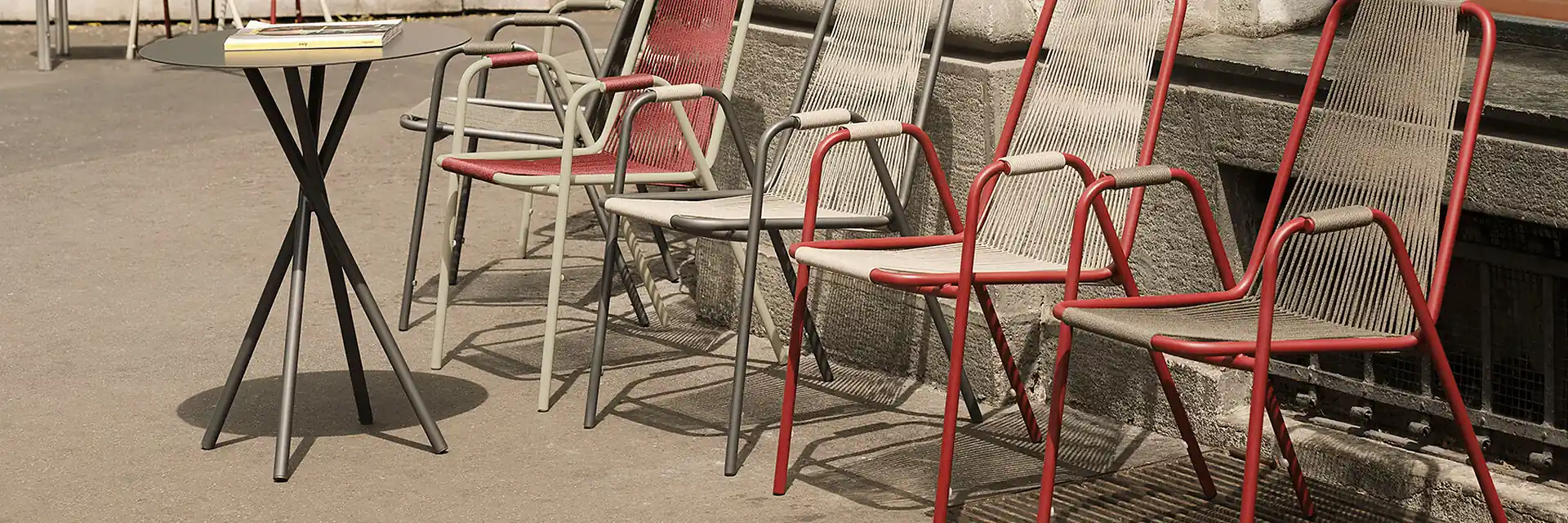 Unopiù Coco chairs in red and natural cord, some stacked, beside a bistro table on a stone pavement
