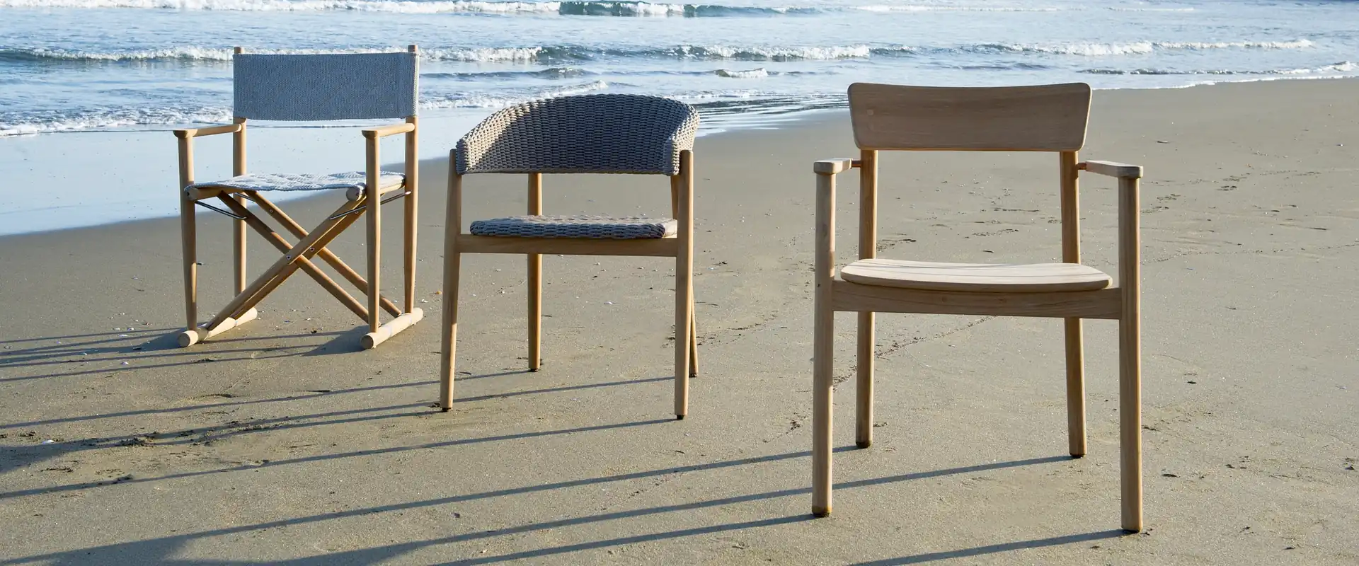 Unopiù Pevero armchair with a woven back between a director's chair and a teak armchair on the sand, with gentle waves behind