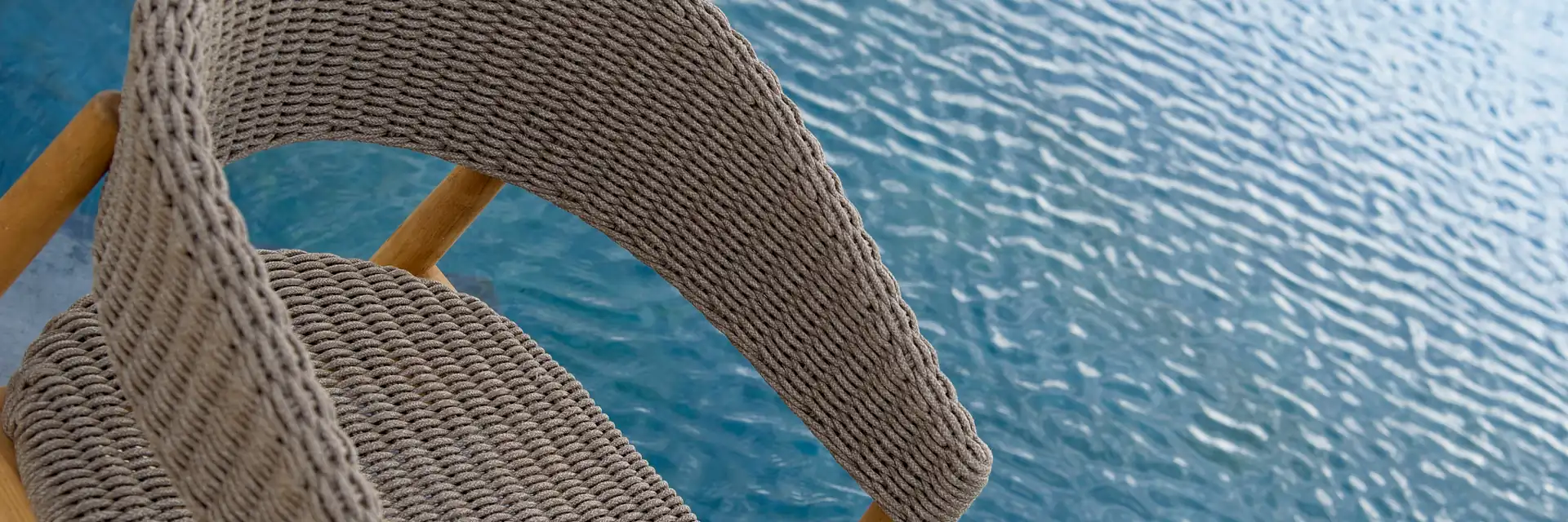 Close view of the woven back and armrest of an Unopiù Pevero armchair above rippling blue water