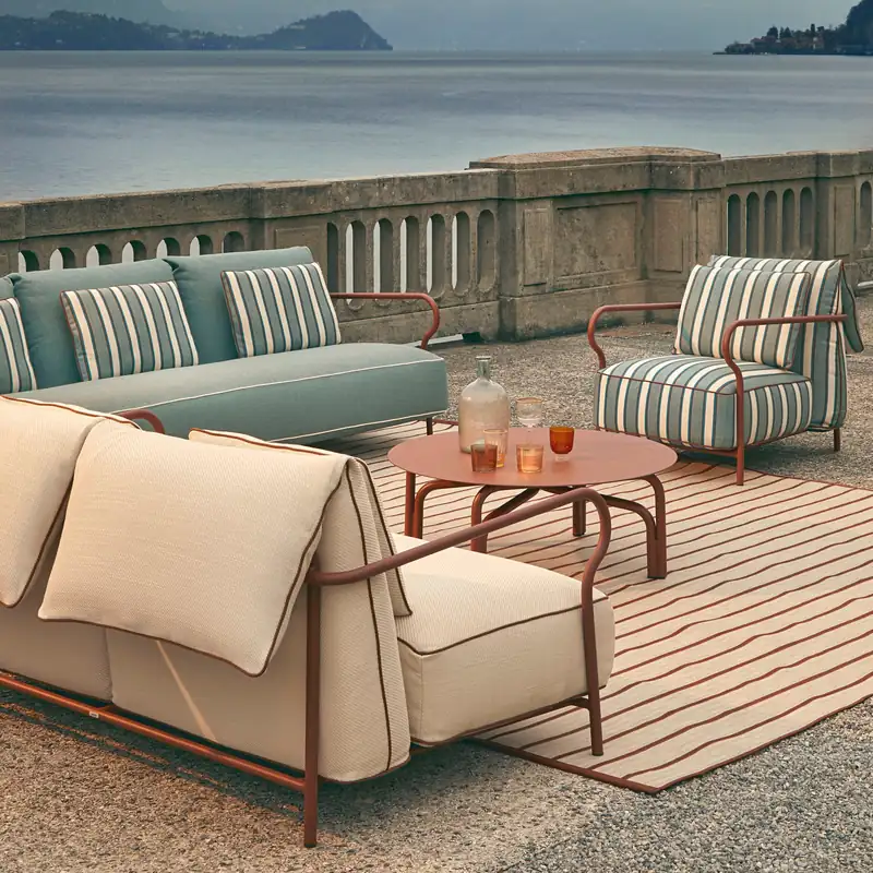 Unopiù Salò sofa with cream cushions and striped armchairs around a round table on a deck above a lake