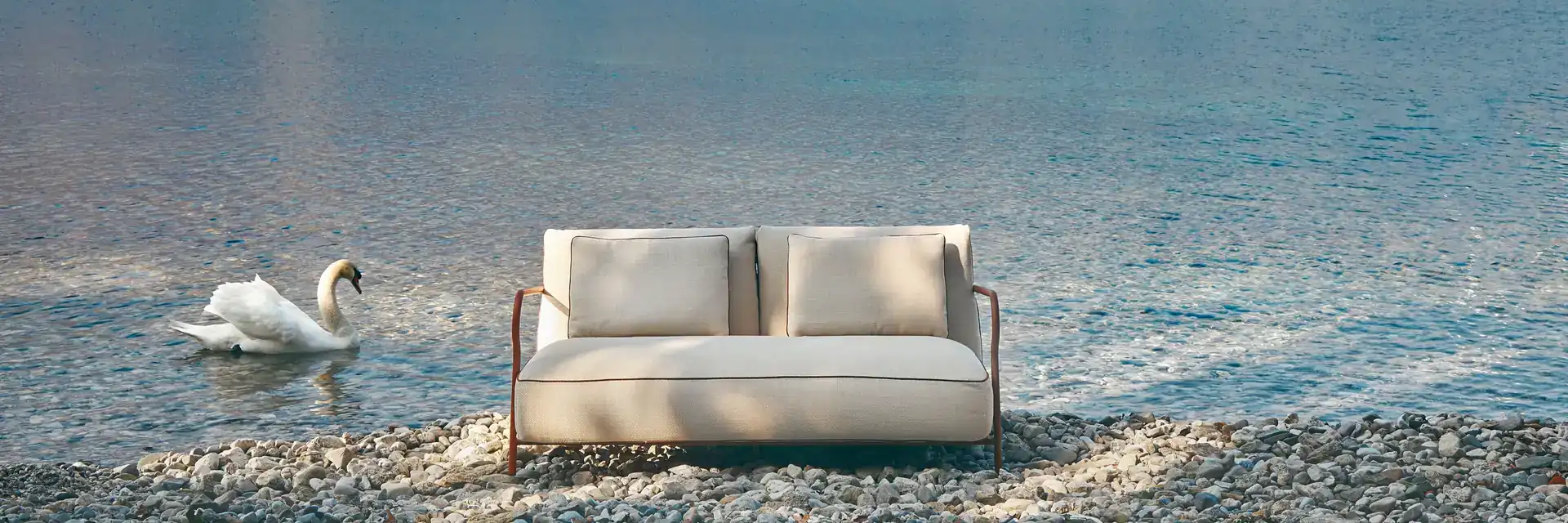 Unopiù Salo sofa on a pebble lakeshore with a swan on the water and mountains across the lake