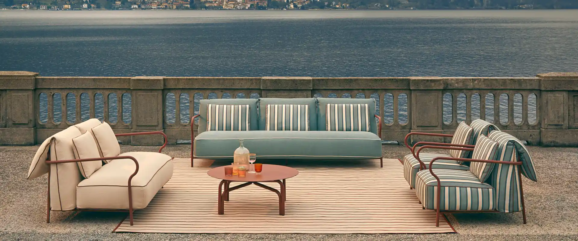Unopiù Salò sofa and armchairs with striped cushions around low tables on a terrace overlooking a lake and mountains