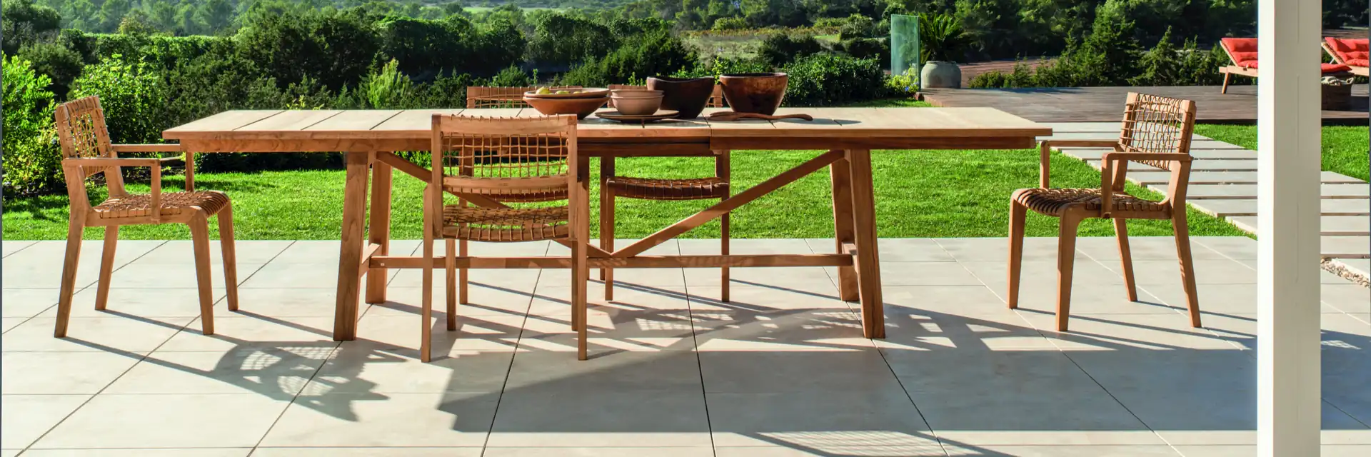 Unopiù Synthesis teak dining table and chairs on a stone terrace overlooking green hills