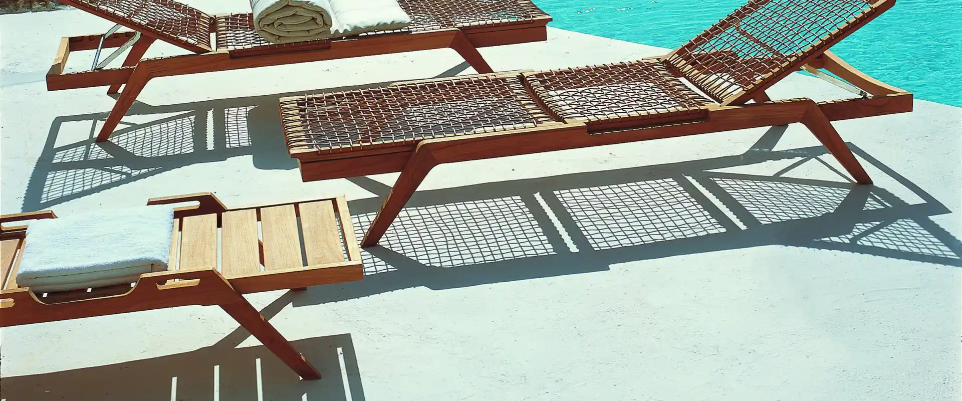 Unopiù Synthesis teak sun loungers with woven seats on a white terrace beside an infinity pool, the sea beyond