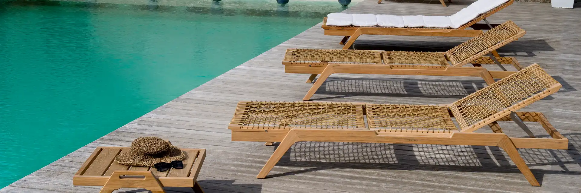 Unopiù Synthesis teak sun loungers and side tables on the timber deck of a pool