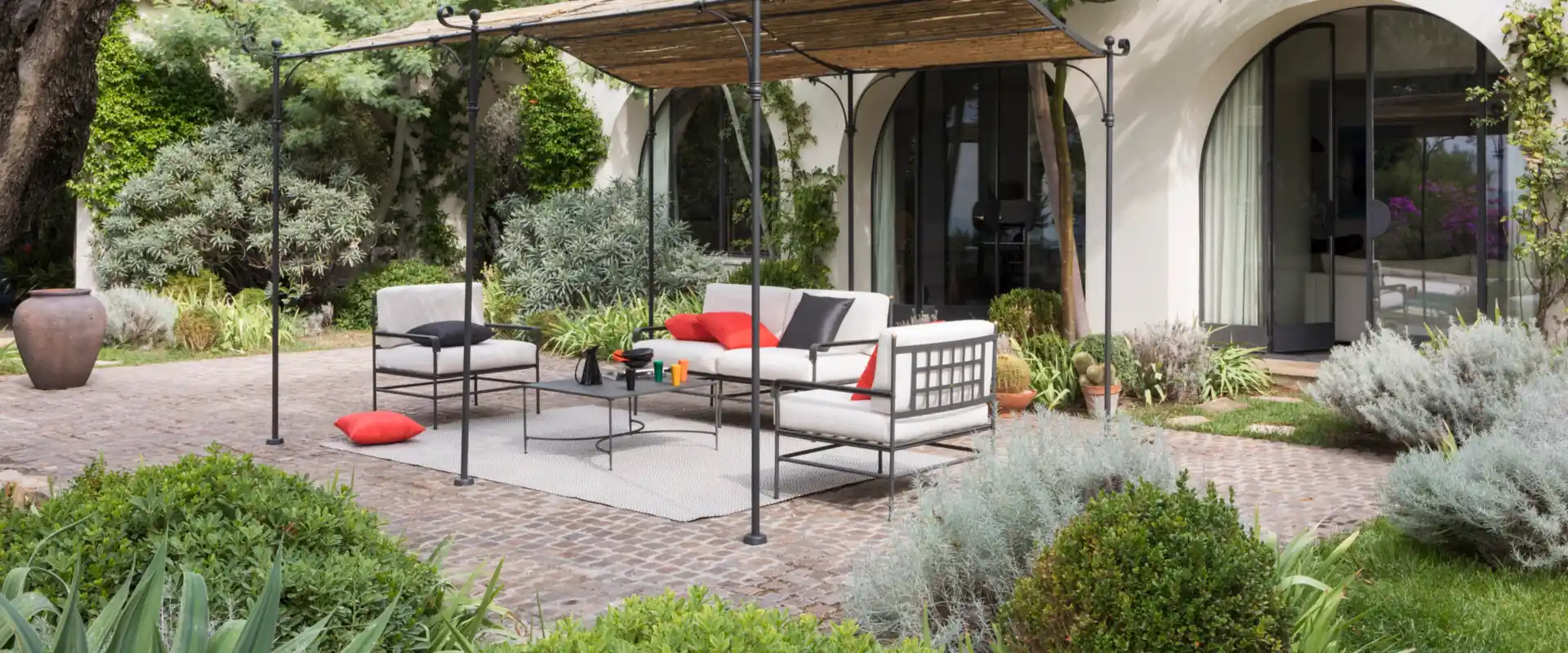 Unopiù Toscana iron sofas and armchairs with white and red cushions in the garden of a villa with arches and a pergola