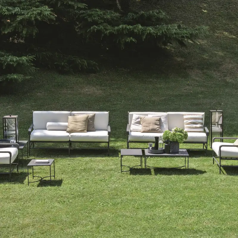 Unopiù Toscana iron sofa, armchairs and coffee table with white cushions on a lawn in front of a hedge