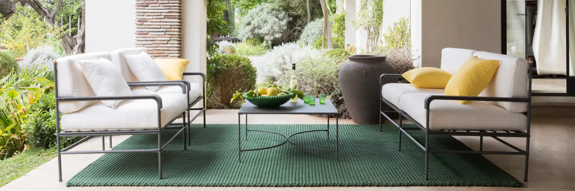 Unopiù Toscana iron sofa and armchairs with white cushions under the arches of a portico opening onto a garden