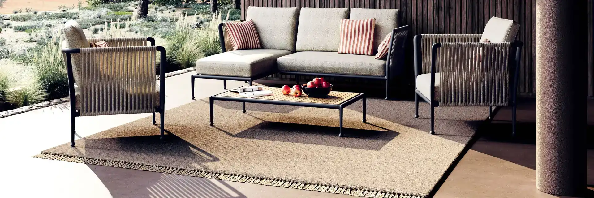 Unopiù Treble sofa and armchairs on a terrace with a dark timber wall, looking out over pines and hills