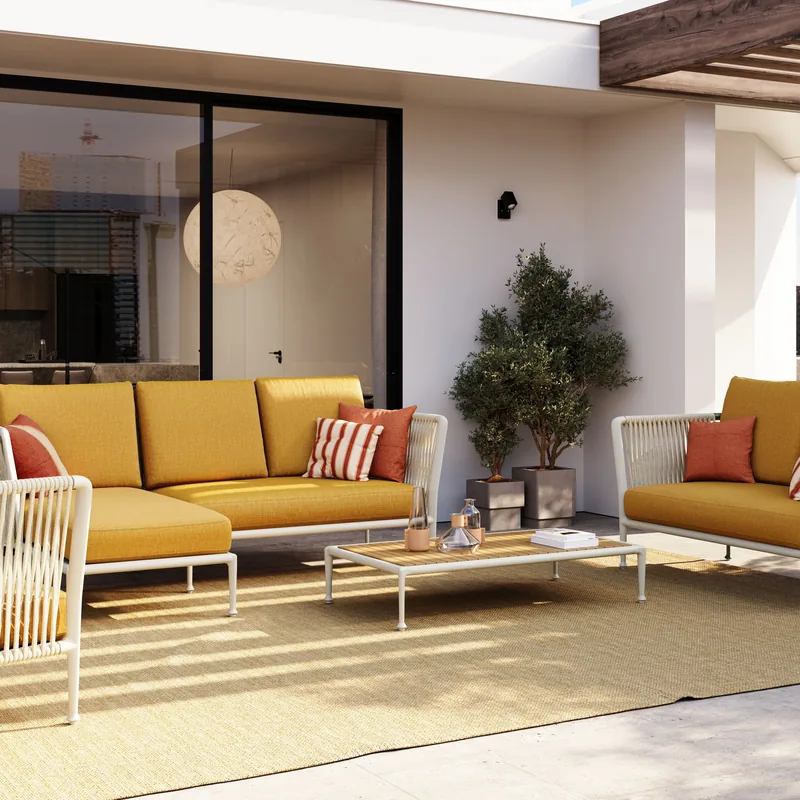 Unopiù Treble corner sofa with mustard-yellow cushions and an armchair in a sunny courtyard with potted trees