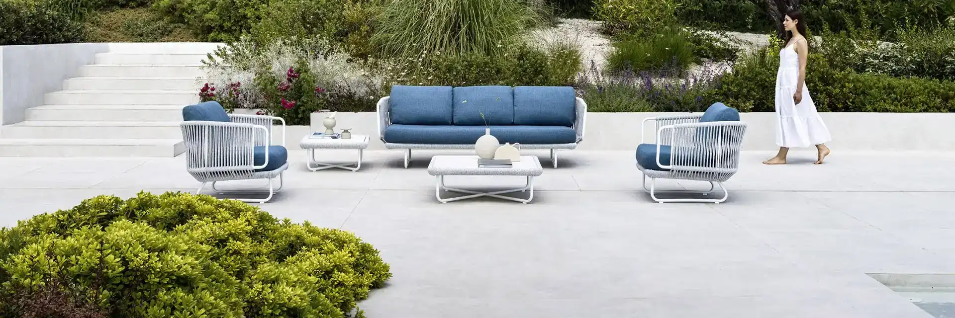Varaschin Babylon sofa and armchairs with blue cushions on a stone terrace beside a garden of olive trees and grasses