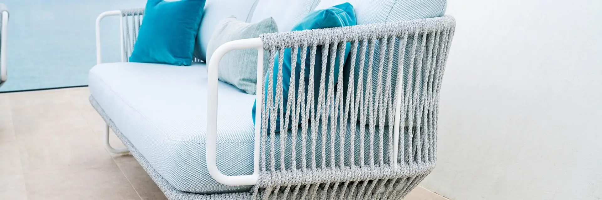 White Varaschin Babylon sofa with a rope-woven frame and turquoise cushions on a white terrace above the sea
