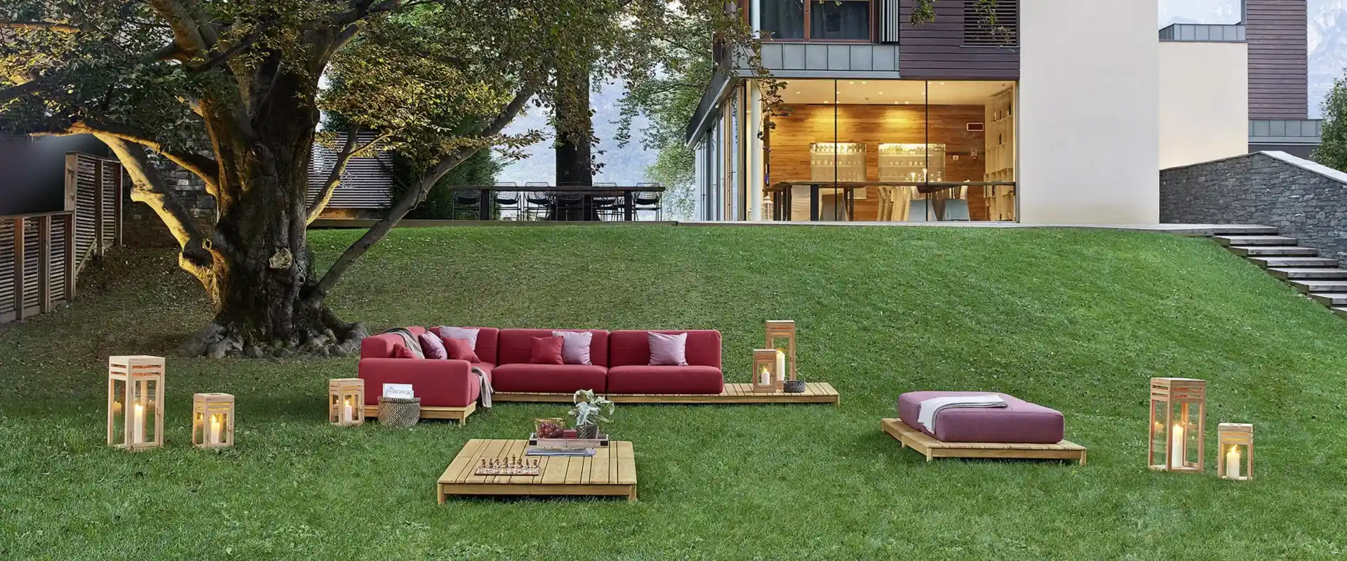 Varaschin Barcode sectional sofa with red cushions and teak platforms on the lawn of a modern villa, with trees behind