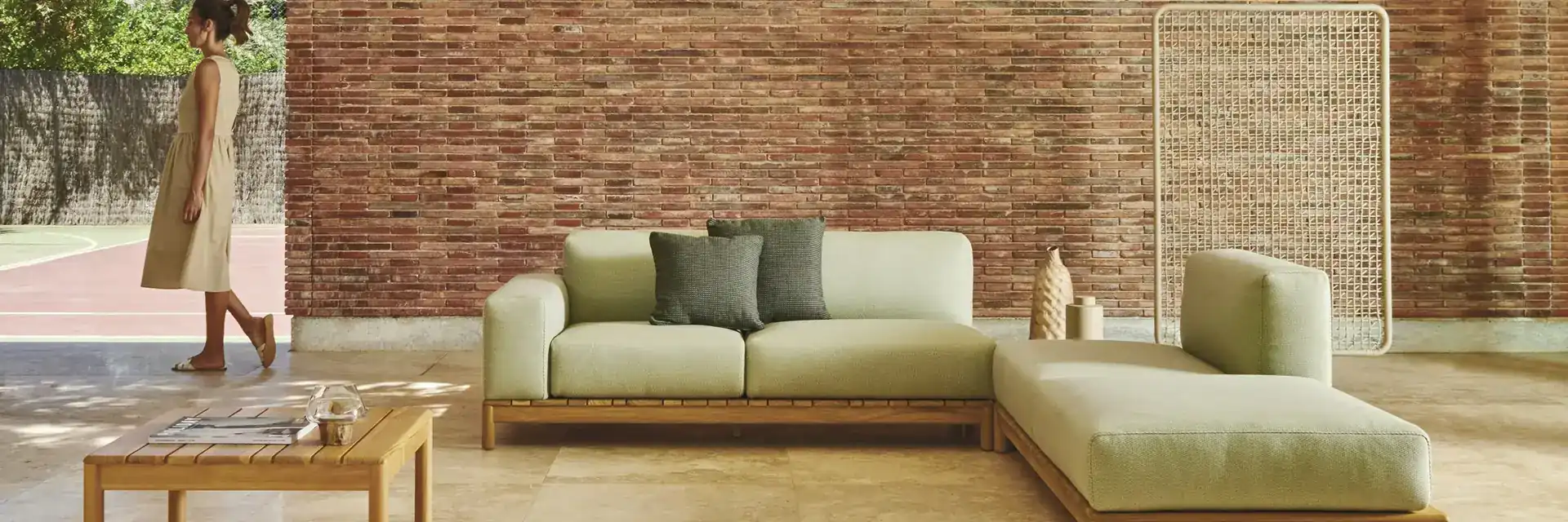 Varaschin Barcode sectional sofa with green cushions and teak low tables on a terrace with a perforated brick wall and a vaulted ceiling