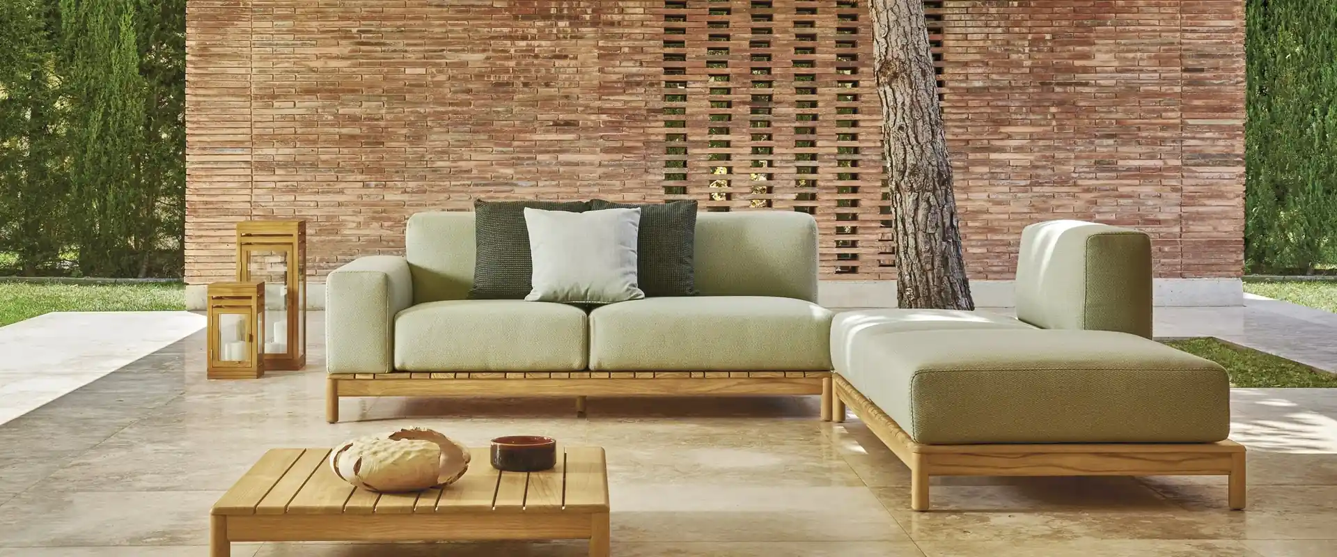 Varaschin Barcode sectional sofa with sage cushions and teak side platforms in a porch with a brick wall, at golden hour