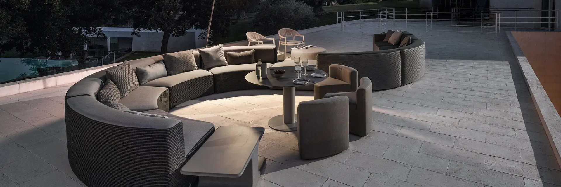 Varaschin Belt curved modular sofa and poufs on the stone terrace of a modern house at dusk