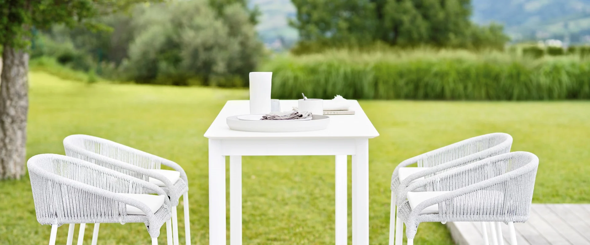 Varaschin Cricket white rope armchairs around a white table on a lawn, with a hedge and hills behind