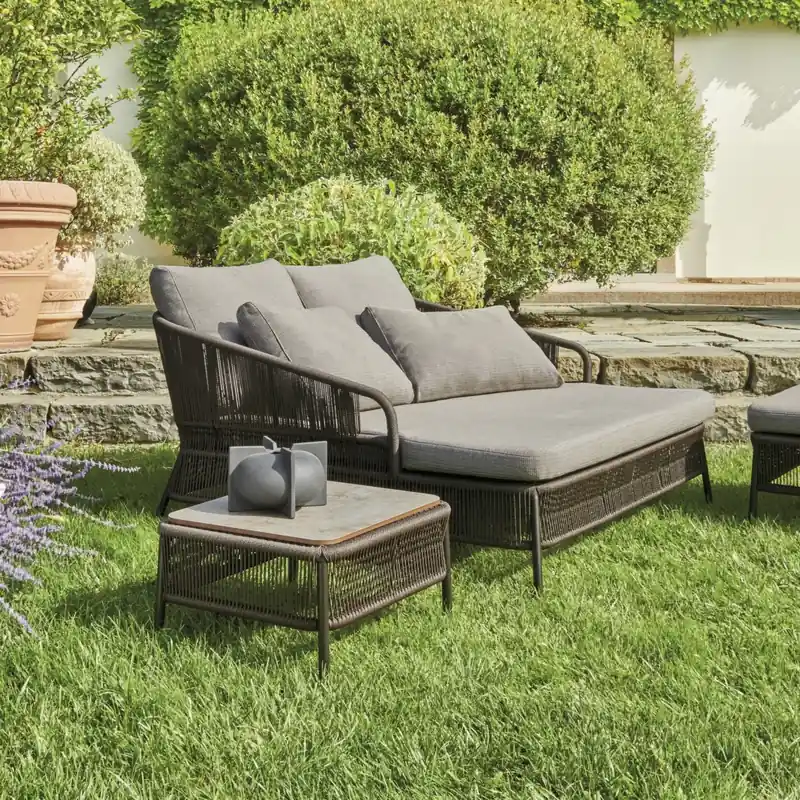 Varaschin Cricket woven lounge sofa with gray cushions and a low table on a lawn, with clipped shrubs and a villa behind