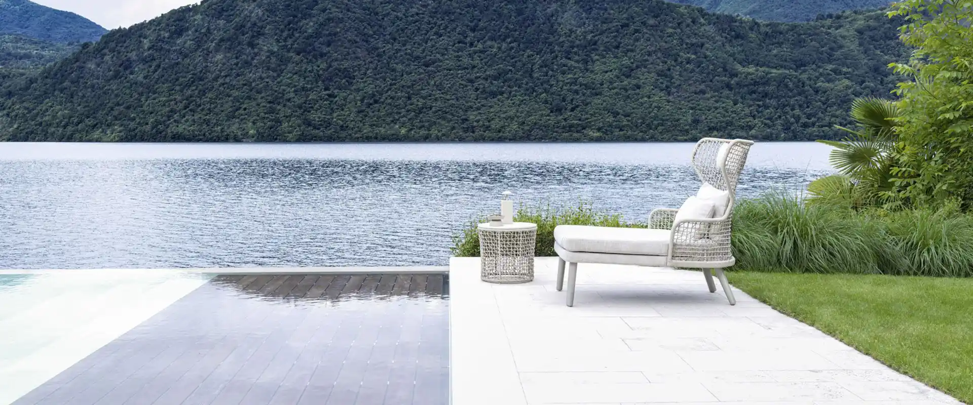 Varaschin Emma armchair in white on a pale terrace at the edge of a still lake, with wooded hills behind