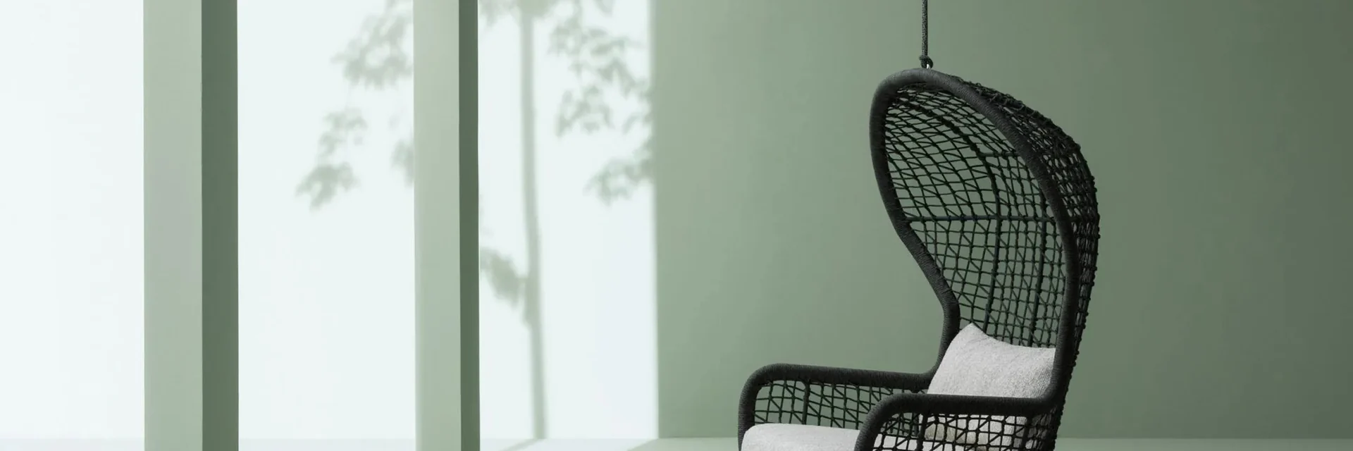 Black Varaschin Emma hanging armchair with a woven shell, suspended in a sage-green room with a tall window
