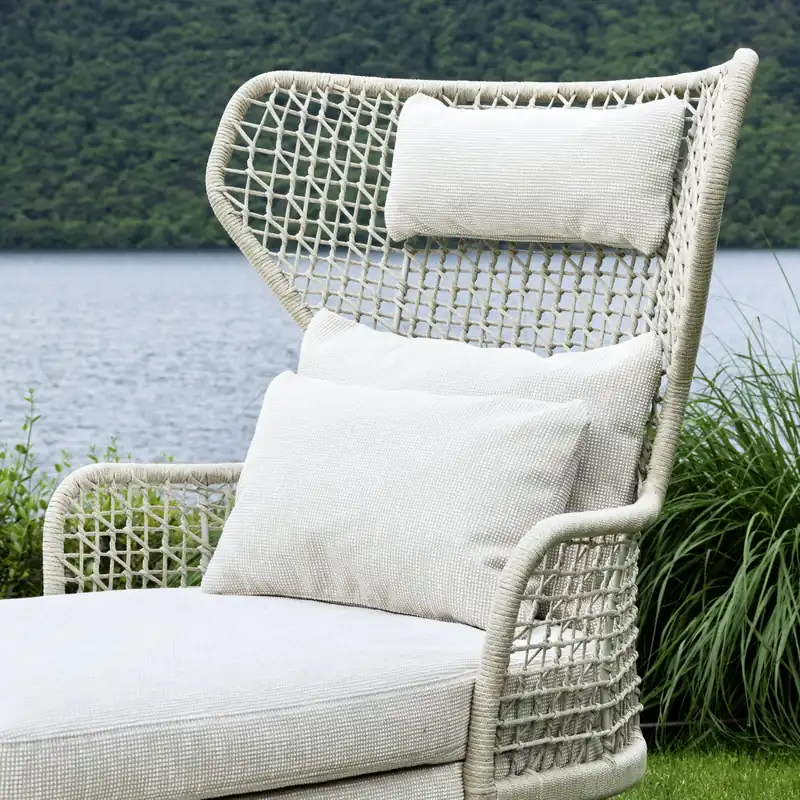 Varaschin Emma high-back armchair in white woven rope with white cushions, in front of a lake and a wooded hill