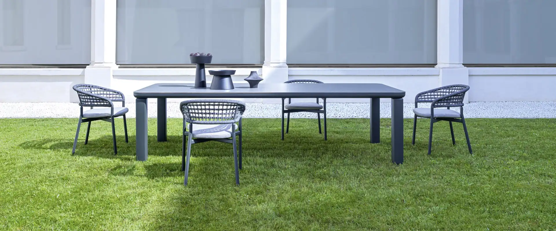Varaschin Plinto dining armchairs around a long table on a lawn, in front of a white arcade with arched windows