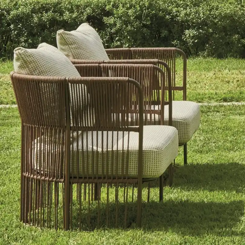 Varaschin Tibidabo armchair with a woven rope frame and pale cushions on a lawn, with shrubs behind